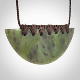 This picture shows a hand carved jade contemporary half-shield pendant. It is a semi-translucent green colour. The cord is hand plaited and adjustable so that you can position the pendant where it suits you best.